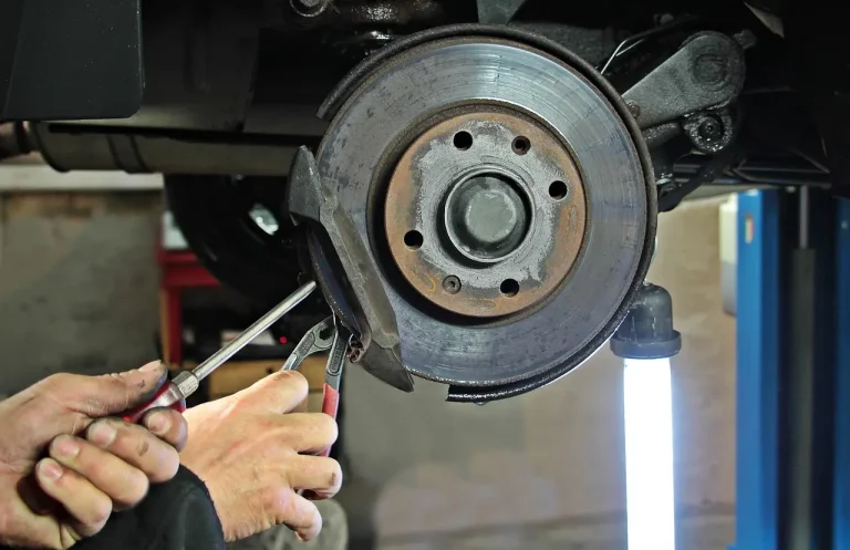 Person measuring brake pad thickness beside a car wheel removed in a home garage