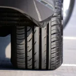 Mechanic measuring a car tire beside a wheel in a bright garage