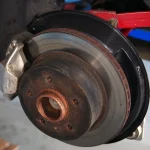 Car wheel with a lightly rusted brake rotor visible through the spokes on a damp morning